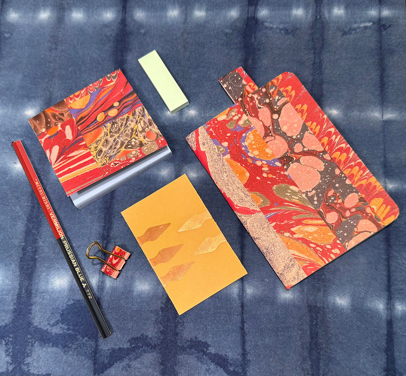 Colorful stationery items including notebooks, a pen, and sticky notes on a textured blue surface.