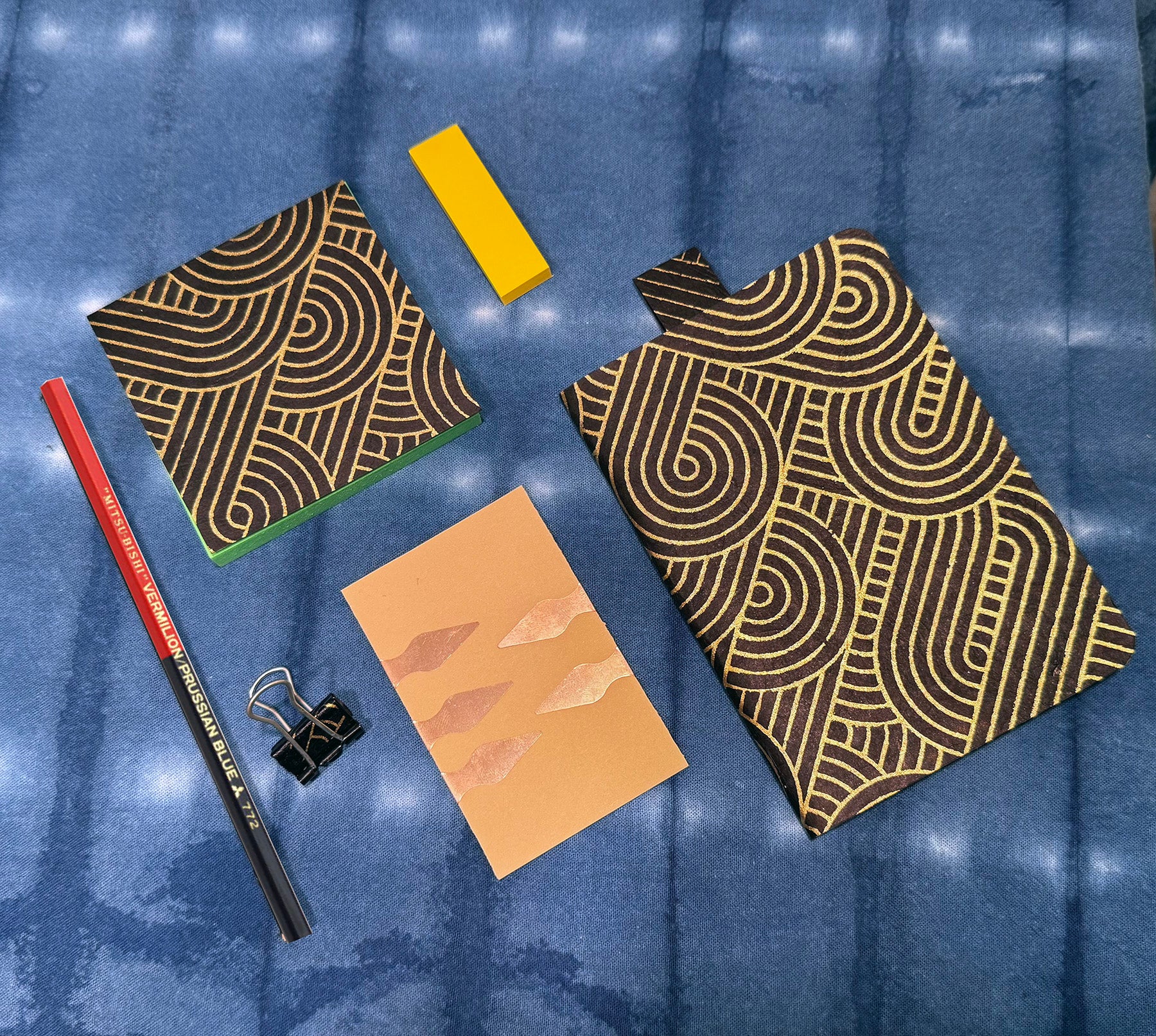 Patterned notebooks, a yellow ruler, a red pencil, and a clip on a blue textured background