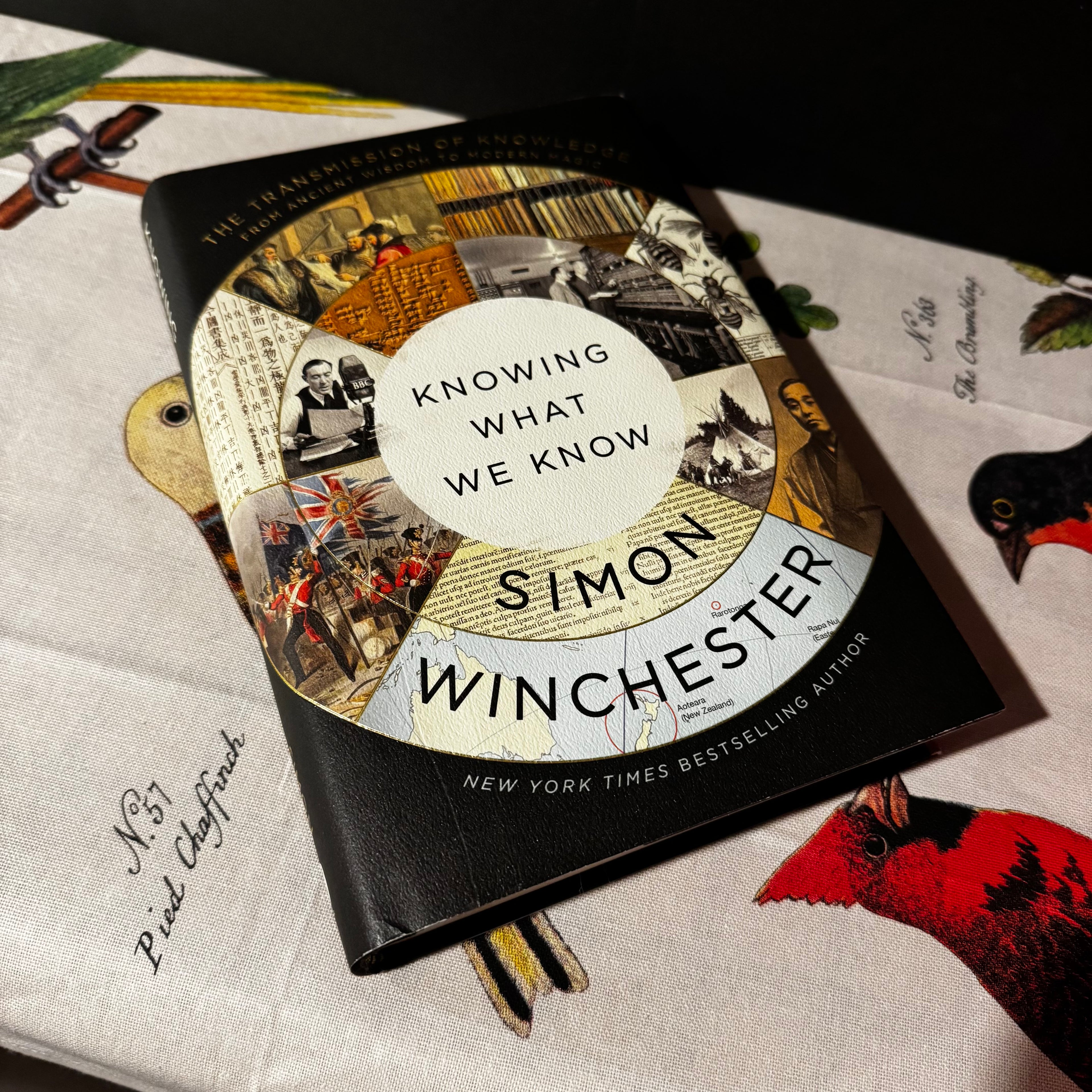 Book titled 'Knowing What We Know' by Simon Winchester on a textured surface with decorative elements.