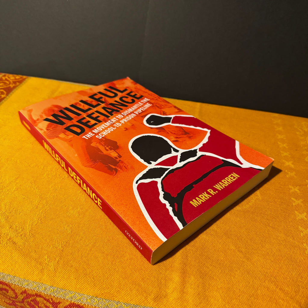 Book titled 'Willeful Defiance' by Mark R. Warren on a yellow surface with a dark background