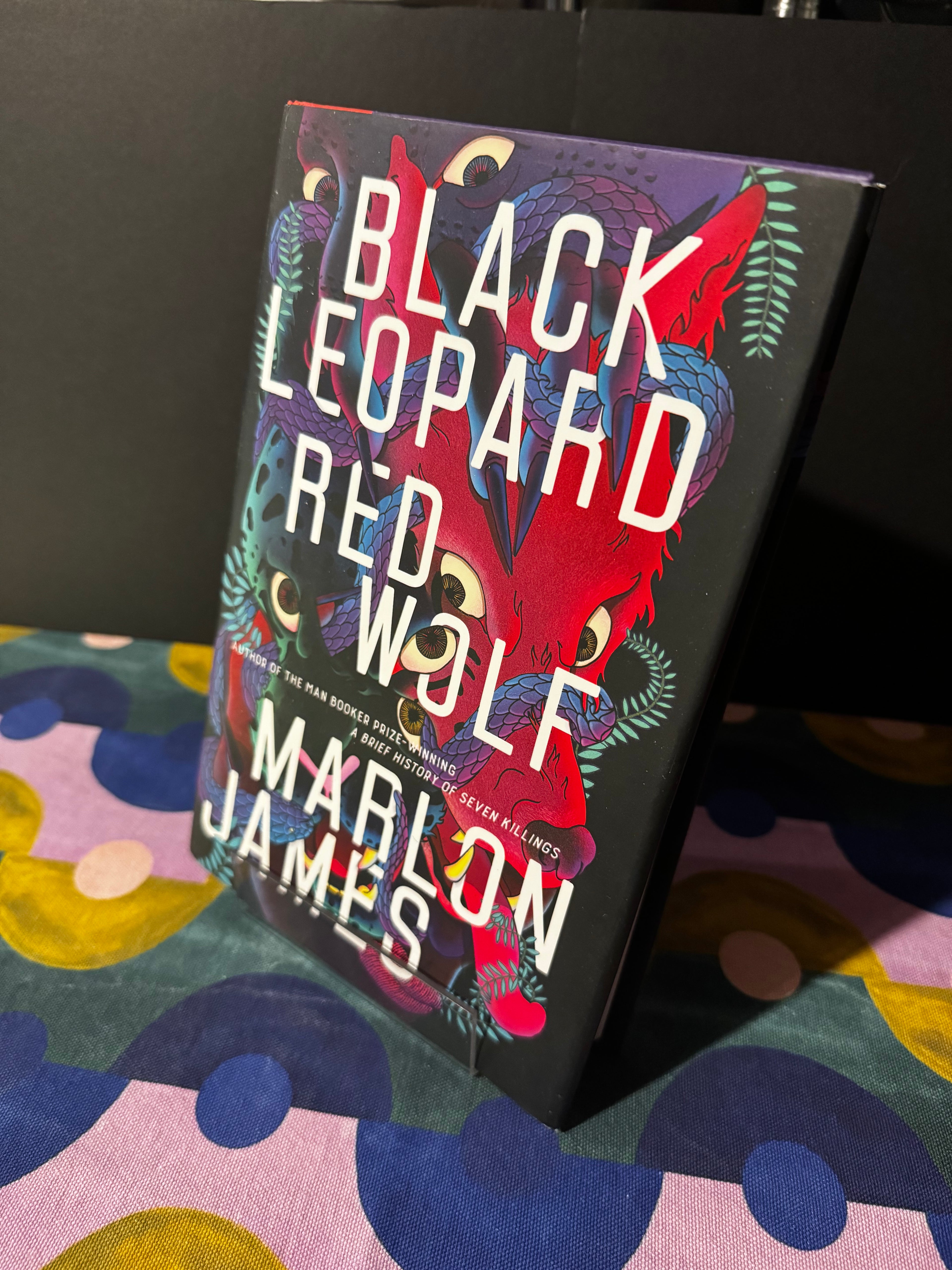Book titled 'Black Leopard, Red Wolf' by Marlon James on a colorful fabric background