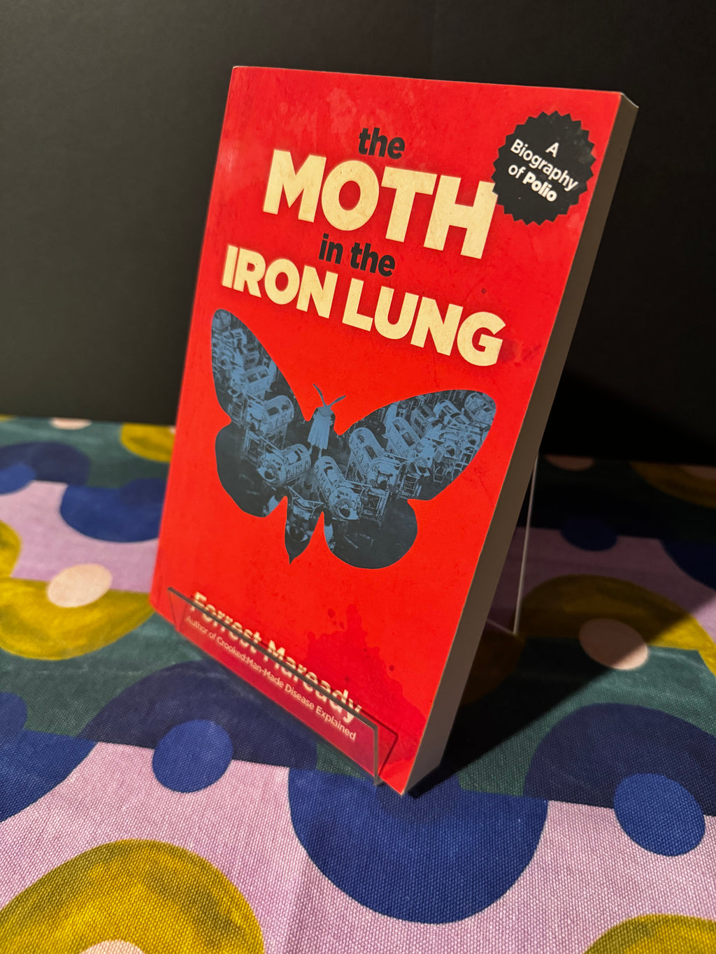 Book titled 'The Moth in the Iron Lung' on a colorful fabric background