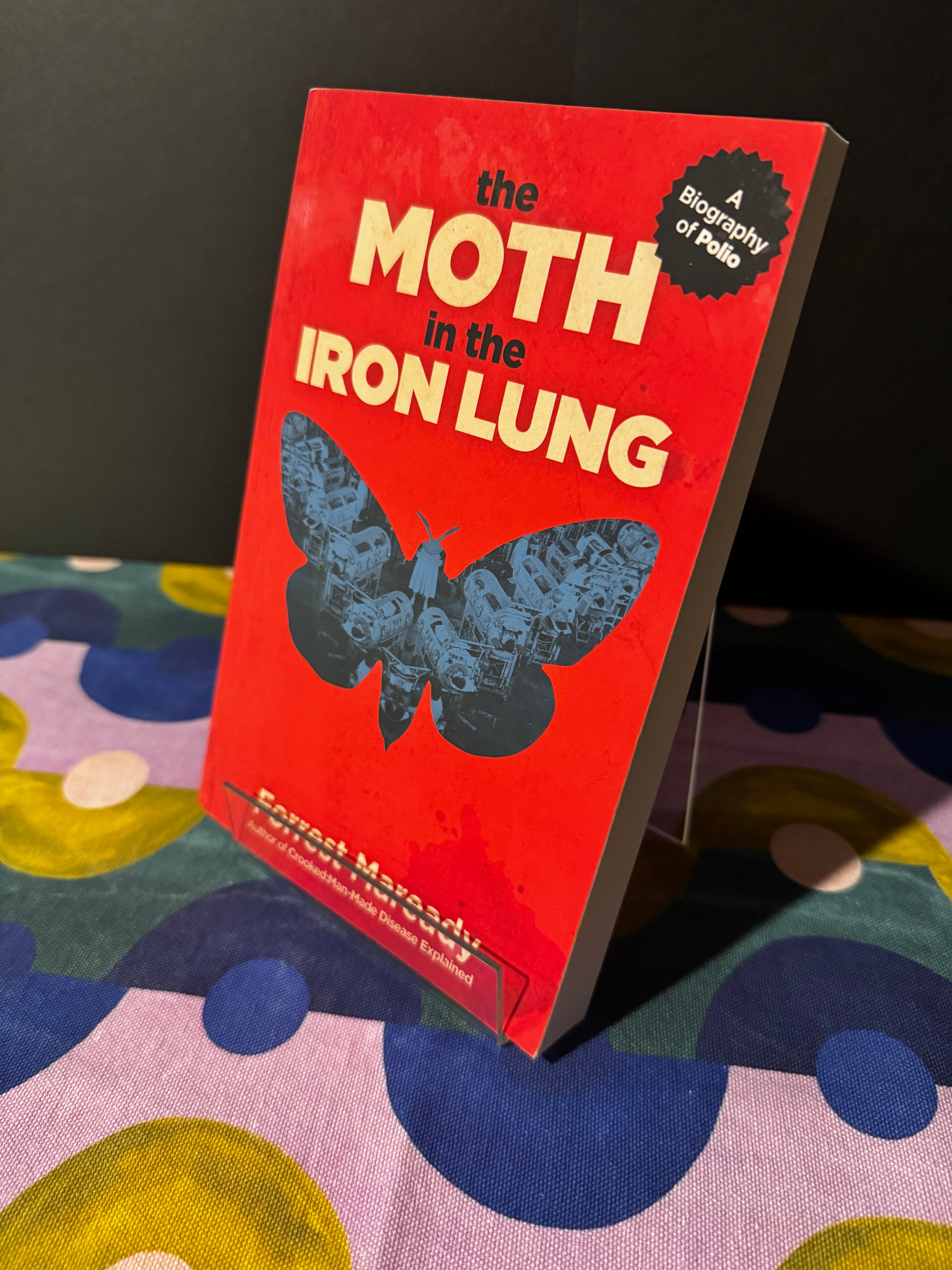 Book titled 'The Moth in the Iron Lung' on a colorful fabric background
