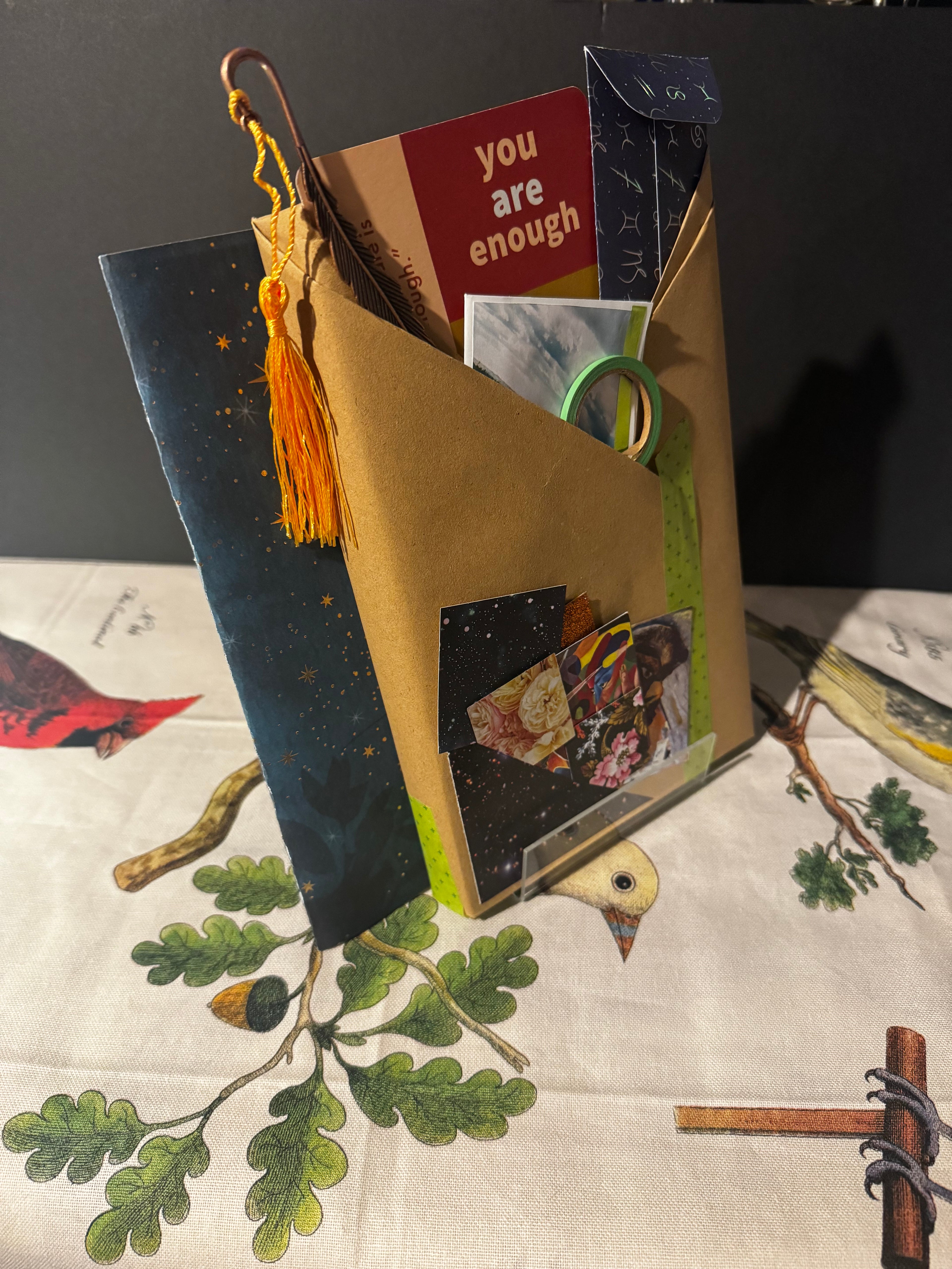 Decorative box with a book, cards, and photos on a tablecloth with nature-themed design.