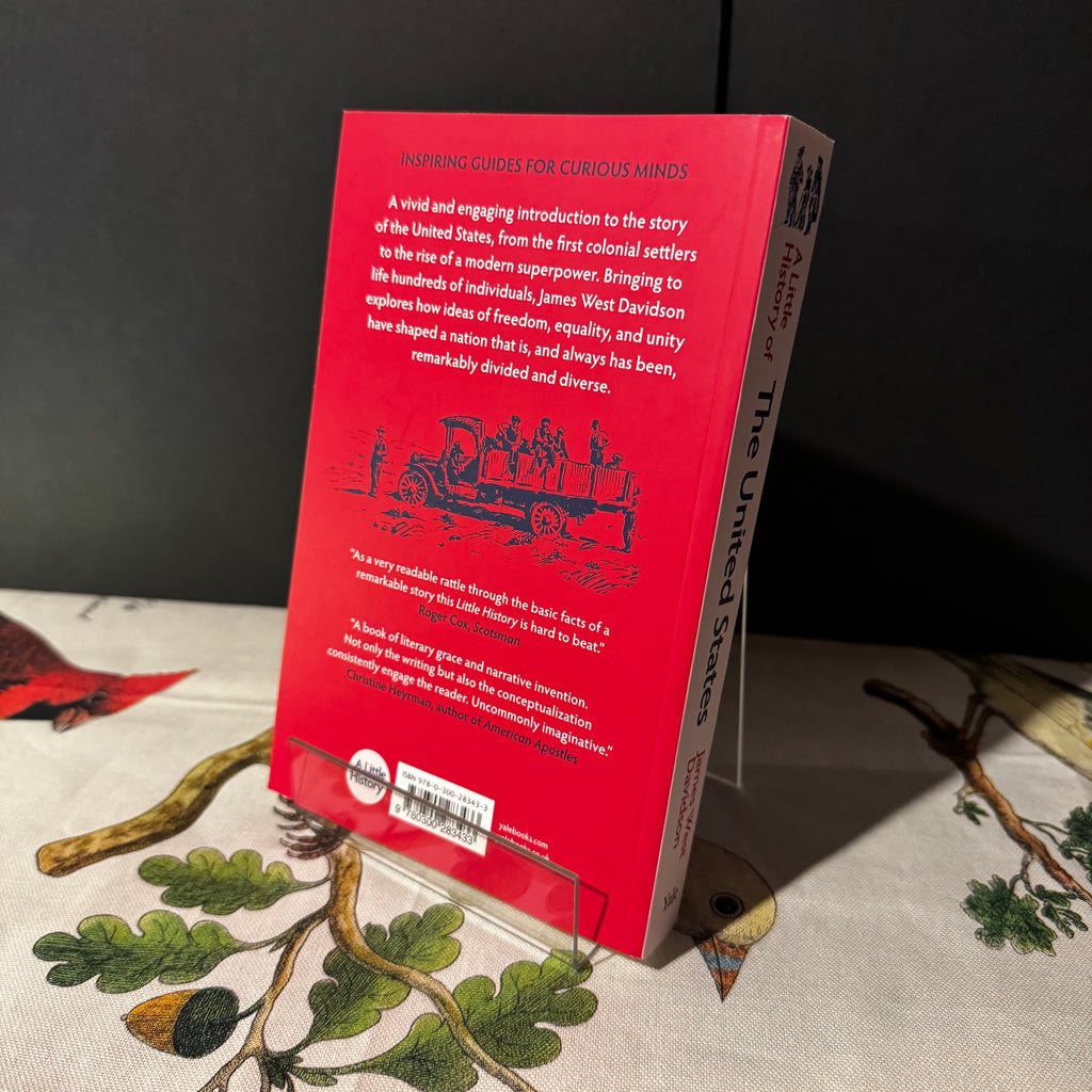 Red book cover with text and illustrations on a tablecloth with nature-themed design