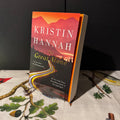 Book titled 'The Great Alone' by Kristin Hannah on a table with a nature-themed cloth.