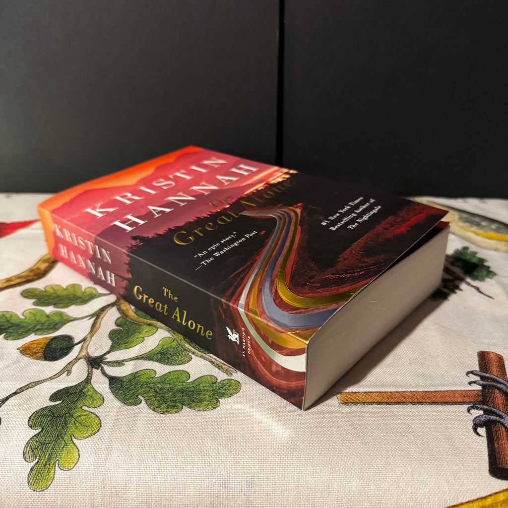 Book titled 'The Great Alone' by Kristin Hannah on a decorative surface with leaves and branches.