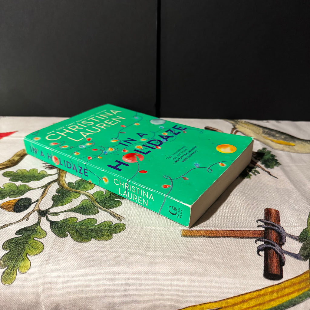 Book titled 'In a Holidaze' by Christina Lauren on a fabric surface with leaf patterns.