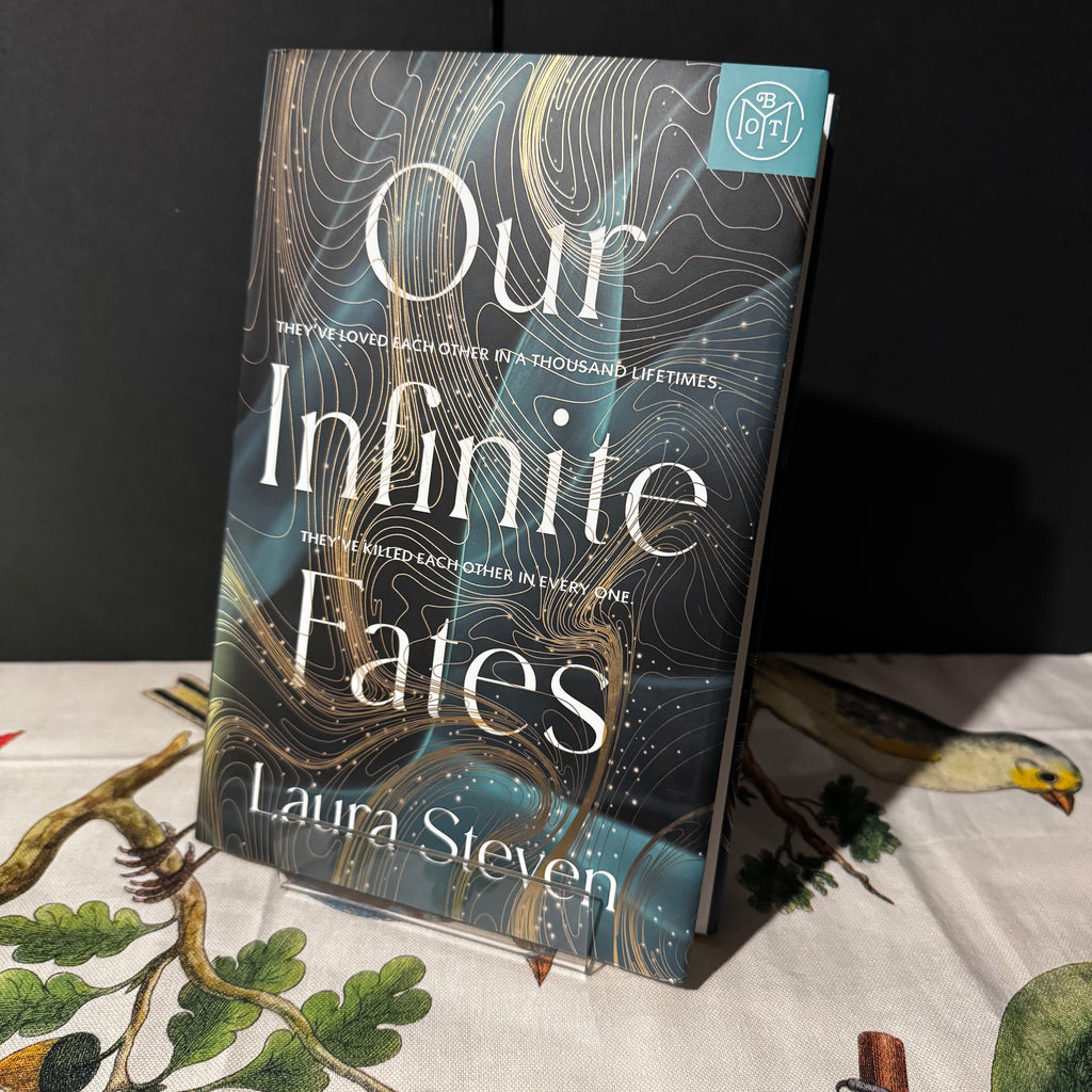 Book titled 'Our Infinite Fates' by Laura Steven on a table with a dark background