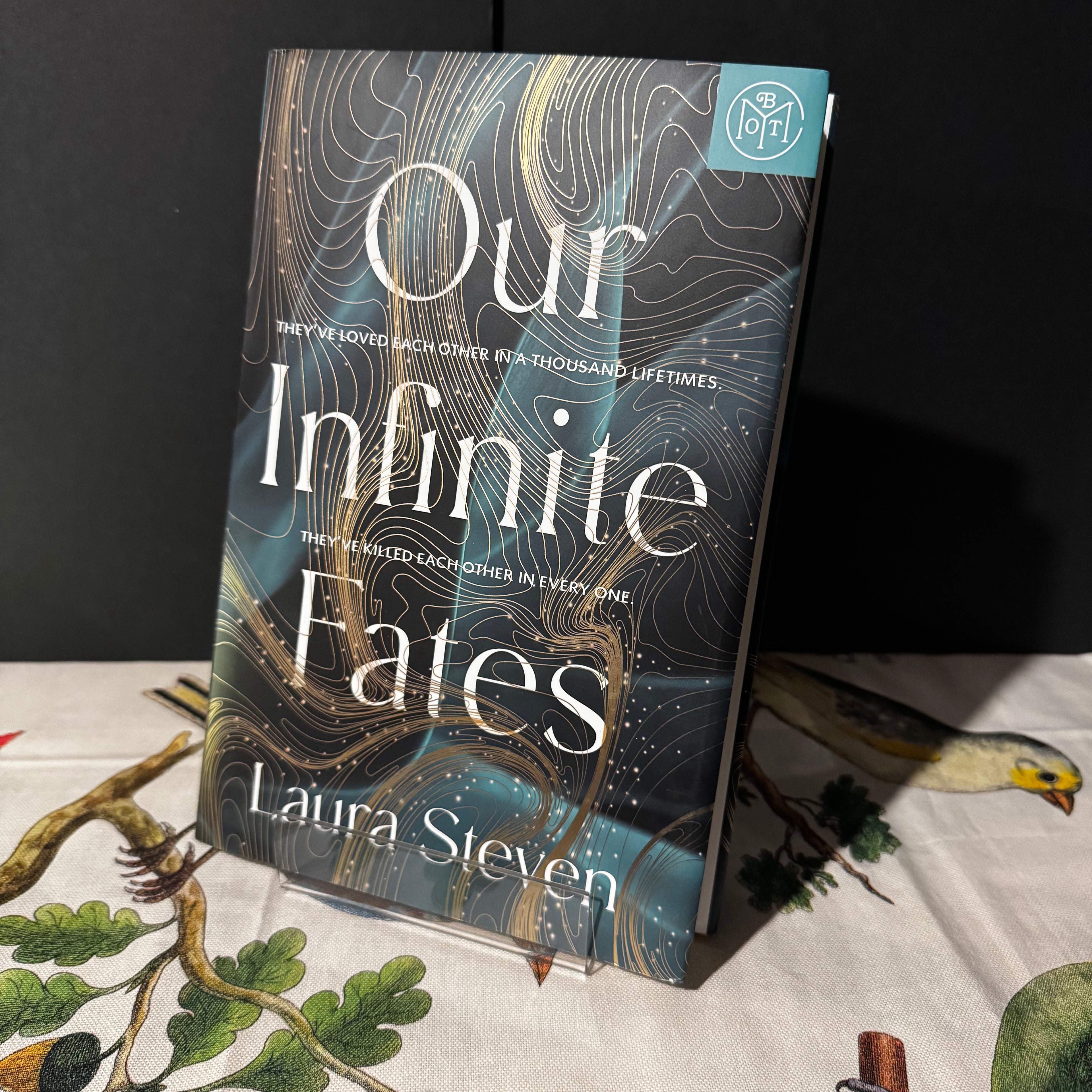 Book titled 'Our Infinite Fates' by Laura Steven on a table with a dark background