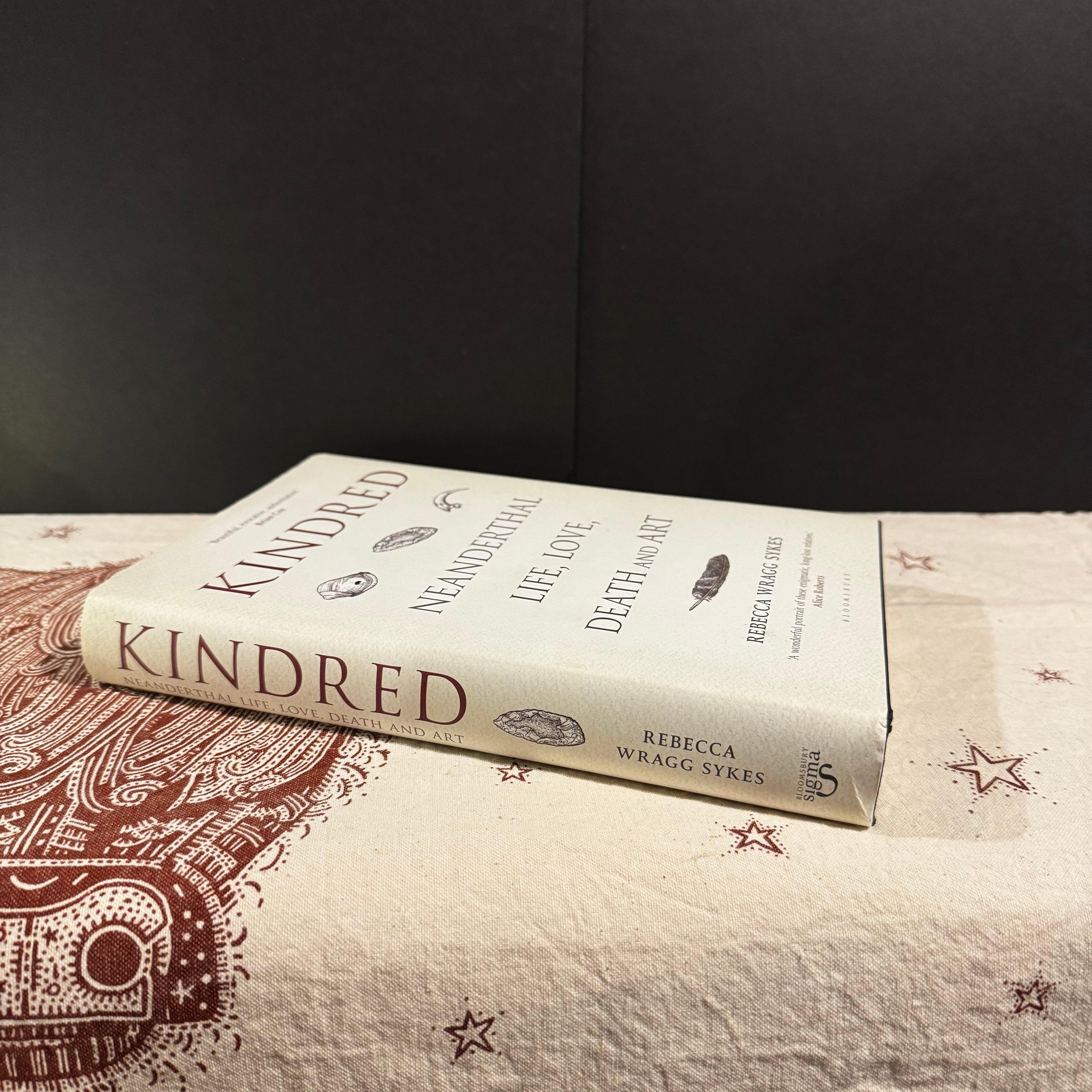 Book titled 'Kindred' by Rebecca Wragg Sykes on a textured surface with a dark background