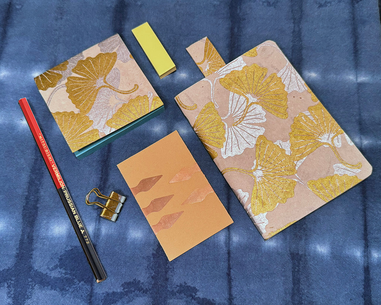 Notebooks with floral design, a pencil, and clips on a blue textured background
