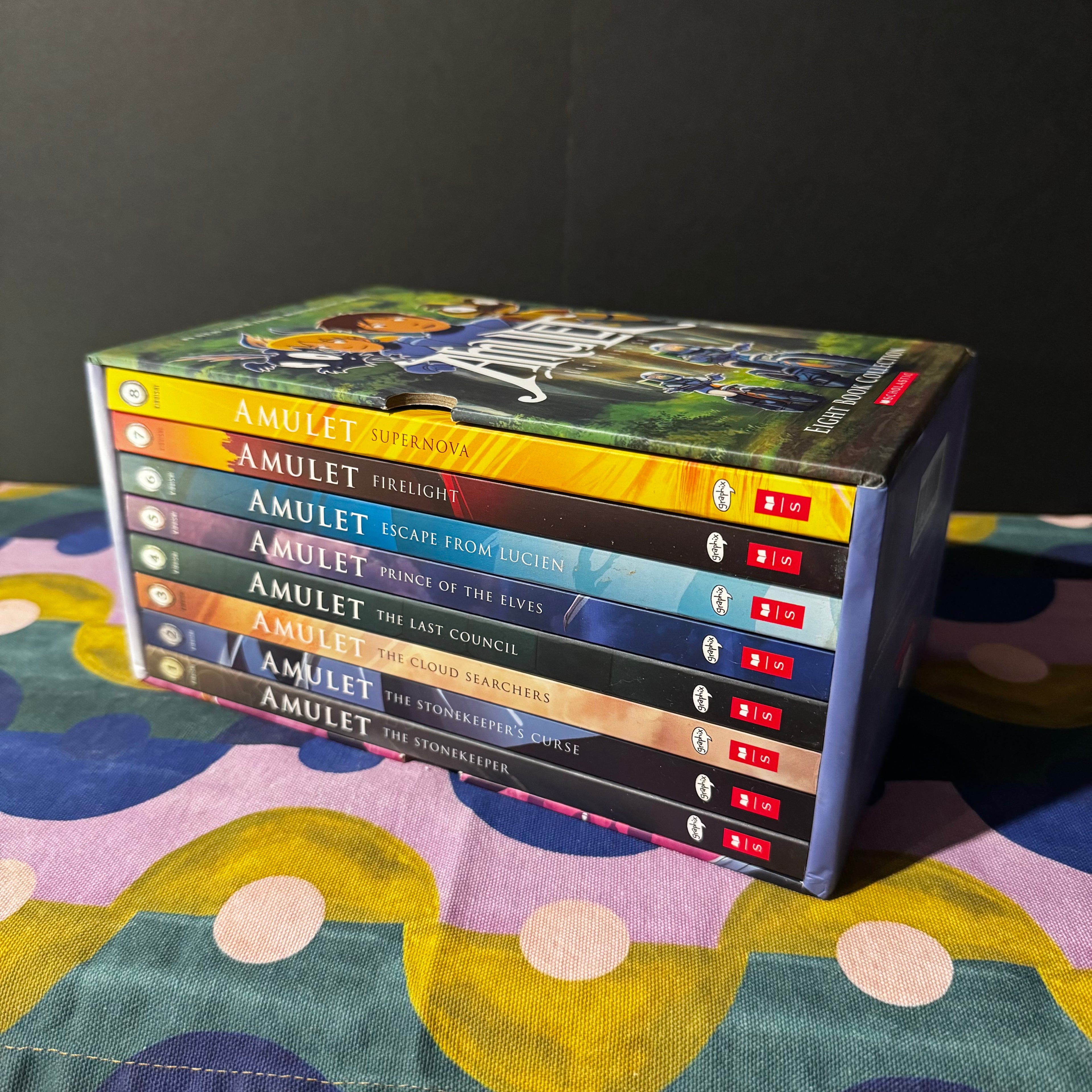 Collection of 'Amulet' books stacked on a colorful surface with a dark background