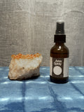 Bottle of 'Area Spray' next to a crystal on a textured surface