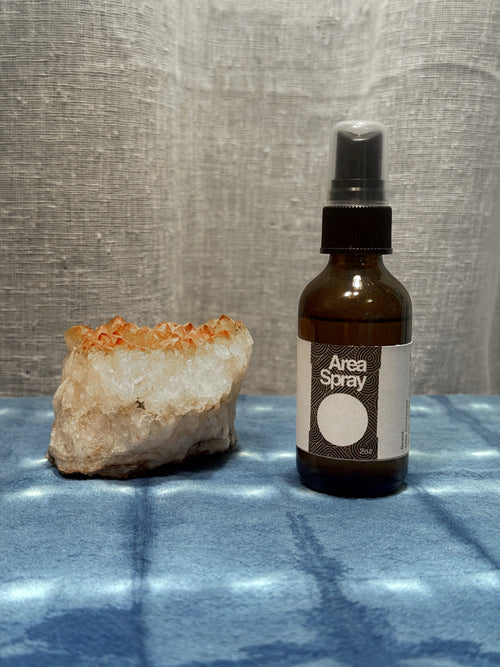 Bottle of 'Area Spray' next to a crystal on a textured surface