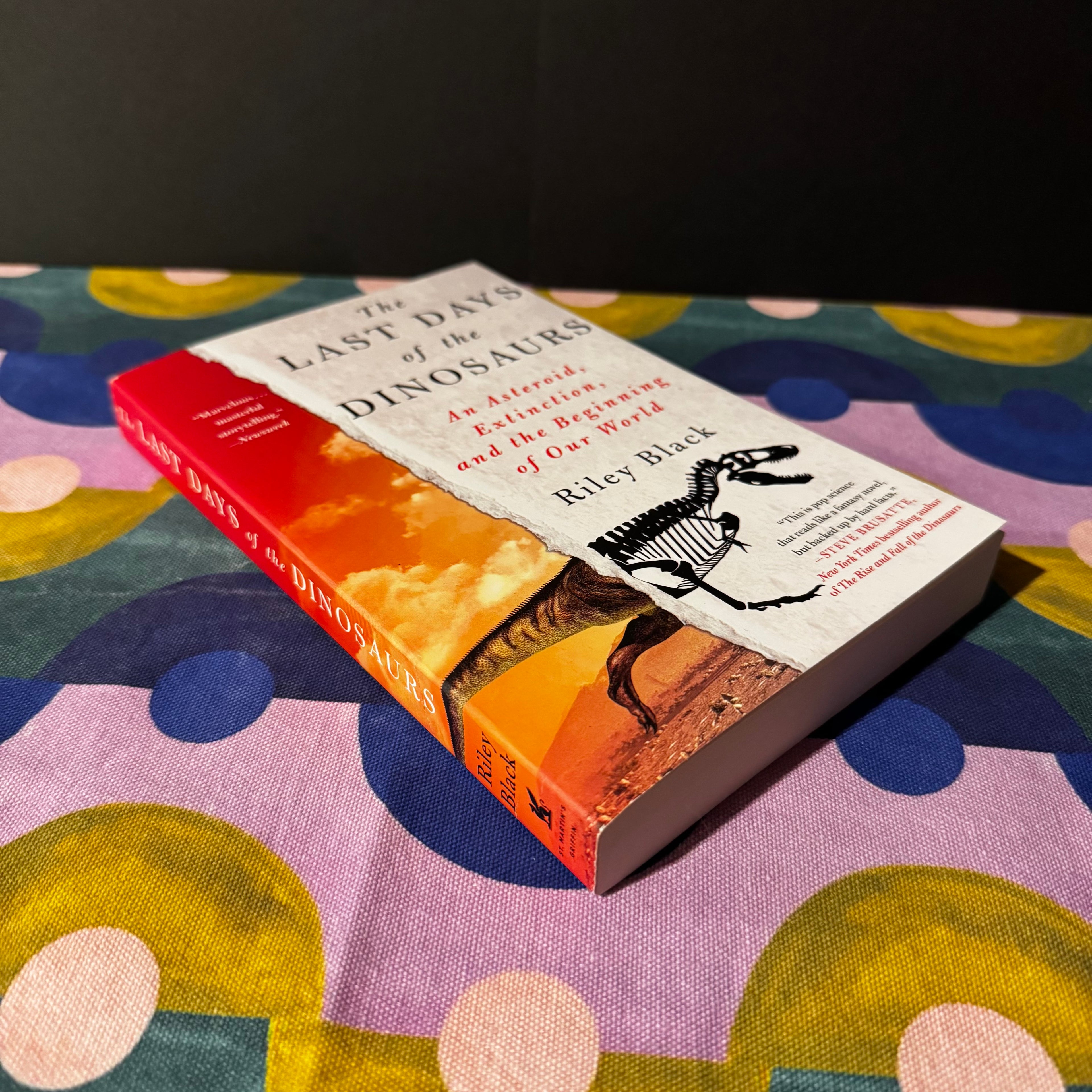 Book titled 'The Last Days of the Dinosaurs' on a colorful fabric background