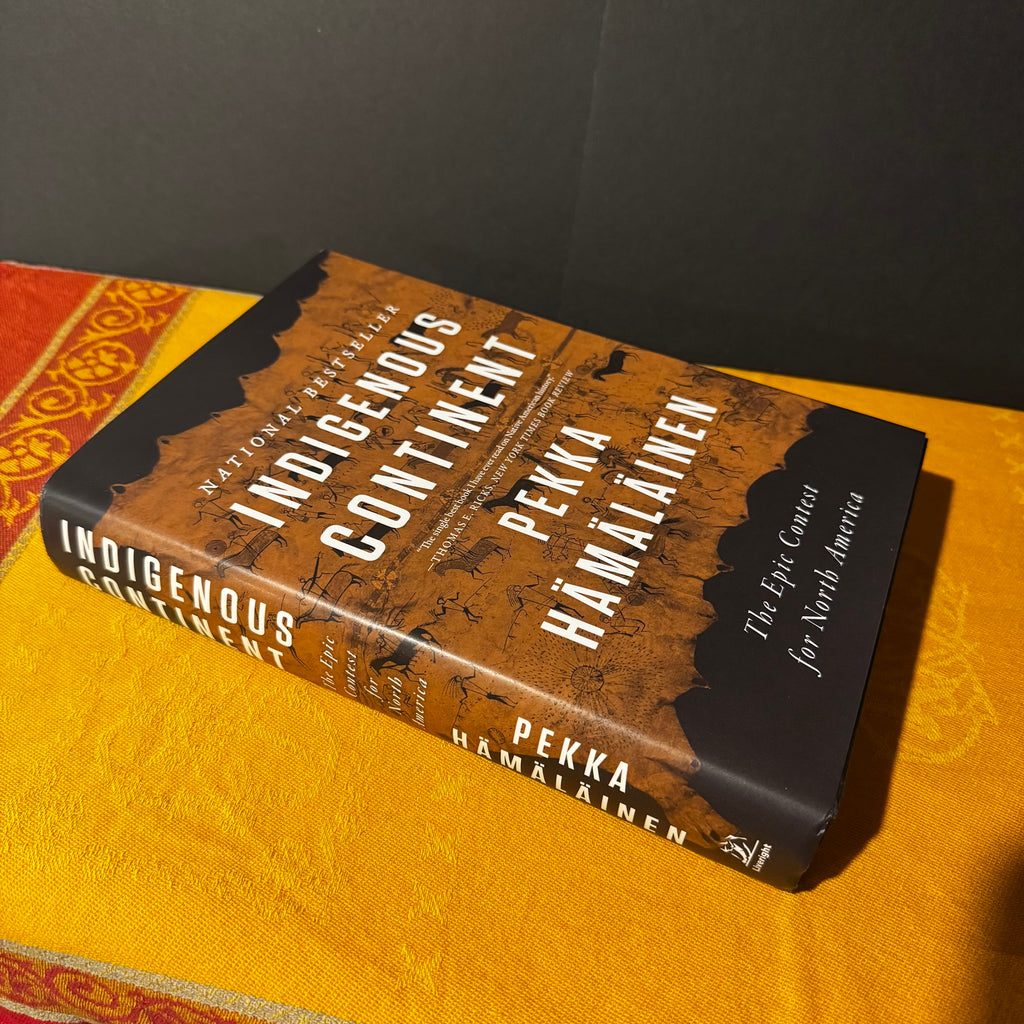 Book titled 'Indigenous Continent' by Pekka Hamalainen on a yellow surface with a dark background