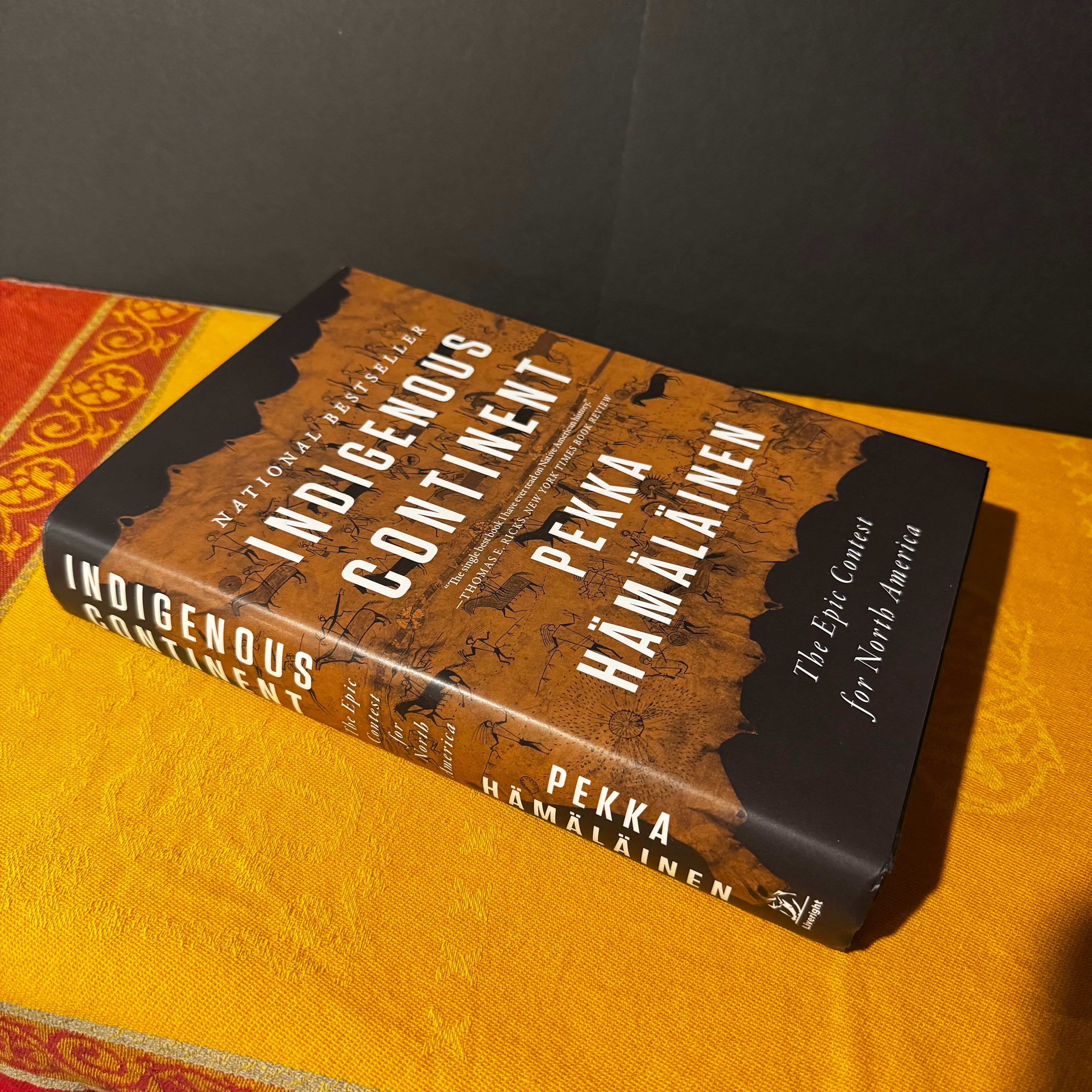 Book titled 'Indigenous Continent' by Pekka Hamalainen on a yellow surface with a dark background